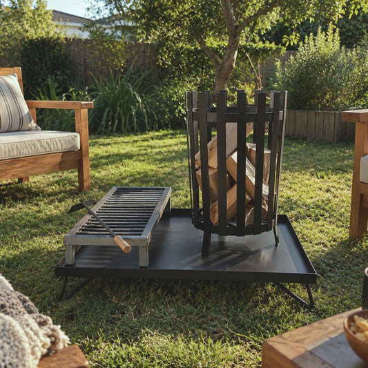 Quemador Industrial con Base XL y parrilla, cargado con leña, en un jardín junto a un sillón