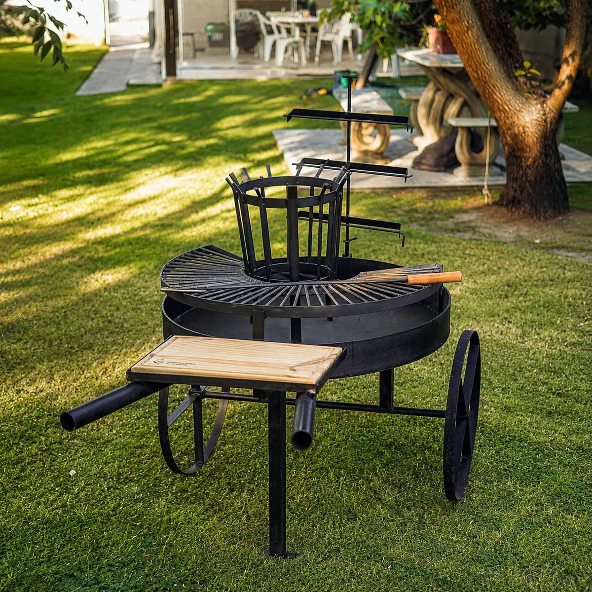 Fogón Criollo 90 en un jardín, junto a un árbol, con la parrilla y la tabla puestas