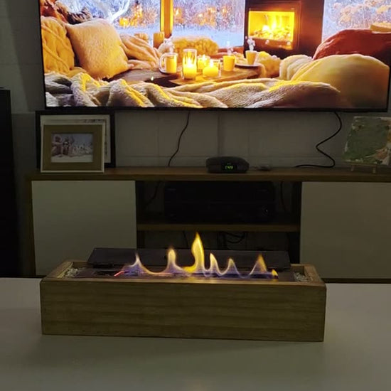 Video de la estufa de bioetanol 40 cm con cajón de madera encendida en una mesa de living, frente a la TV