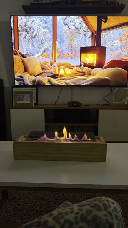 Video de la estufa de bioetanol 40 cm con cajón de madera encendida en una mesa de living, frente a la TV