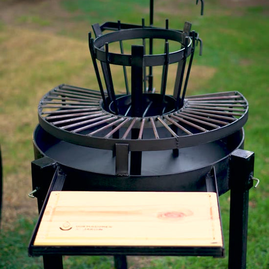 Video del Fogón Criollo 60 de hierro con parrilla circular, cruz con ganchos y tabla de madera, en un jardín