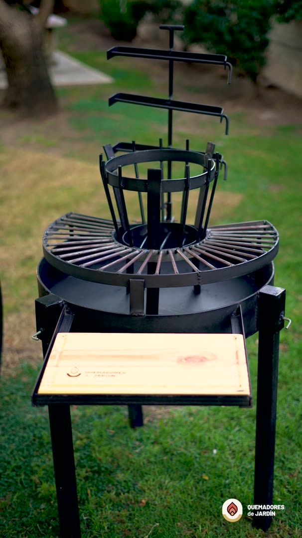 Video del Fogón Criollo 60 de hierro con parrilla circular, cruz con ganchos y tabla de madera, en un jardín